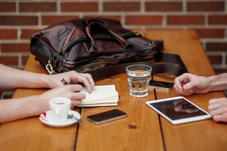 Two people sit at a wooden table with devices and drinks, discussing plans for a full-service specialty contractor.