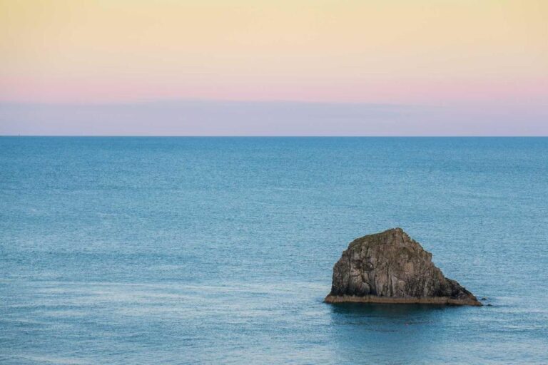A large rock sits in calm blue ocean water under a pastel sky, like a full-service specialty contractor steady amidst changing horizons.