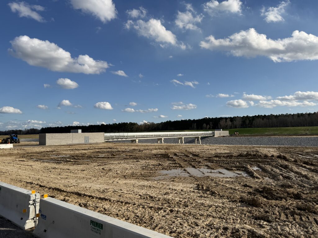 A construction site with a dirt lot, concrete barriers, and a partially built structure by a full-service specialty contractor under a blue sky.